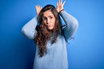 Young beautiful woman with curly hair wearing blue casual sweater over isolated background Doing...