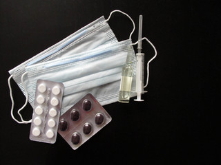 Medical masks with tablets, ampoule and syringe on a black background. Creating a vaccine against coronavirus. Covid19 virus, coronavirus and epidemic content. Copy space