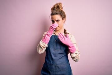 Young beautiful blonde cleaner woman doing housework wearing arpon and gloves smelling something...