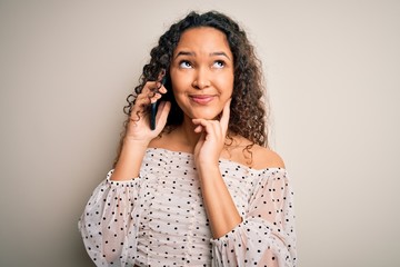 Young beautiful woman with curly hair having conversation talking on the smartphone serious face thinking about question, very confused idea