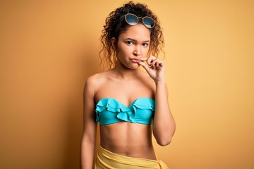 Young beautiful american woman on vacation wearing bikini over isolated yellow background mouth and...