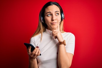 Young beautiful brunette woman listening to music using smartphone and headphones serious face thinking about question, very confused idea