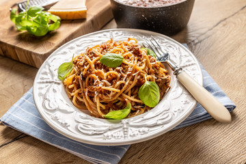 Italian pasta spaghetti bolognese served on white plate with parmesan cheese and basil