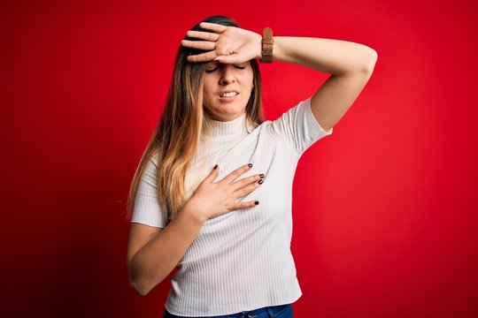 Beautiful blonde woman with blue eyes wearing casual white t-shirt over red background Touching forehead for illness and fever, flu and cold, virus sick