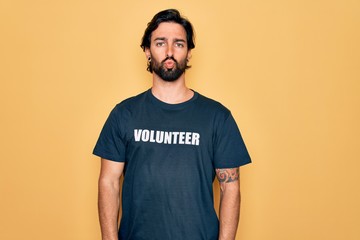 Young handsome hispanic volunteer man wearing volunteering t-shirt as social care looking at the...