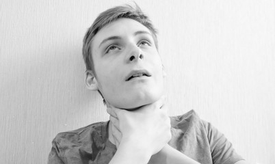 Teen boy holds himself by the throat and suffocates on a light background