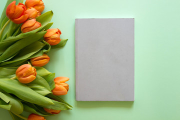 Grey notepad and orange tulips with green leaf  on green background. Spring time is in the air, smart working.