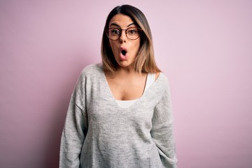 Fototapeta premium Young beautiful brunette woman wearing casual sweater and glasses over pink background afraid and shocked with surprise expression, fear and excited face.