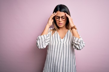 Young beautiful woman wearing casual striped t-shirt and glasses over pink background with hand on headache because stress. Suffering migraine.