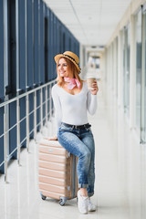 Young pretty stylish woman with luggage at the international airport. Waiting her flight at tax free shopping zone.