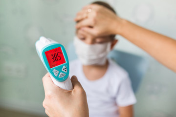 Girl doctor measures the body temperature of a small boy in a medical mask with an electronic thermometer. High fever from the virus in the child.