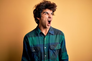 Young handsome man wearing casual shirt standing over isolated yellow background angry and mad screaming frustrated and furious, shouting with anger. Rage and aggressive concept.