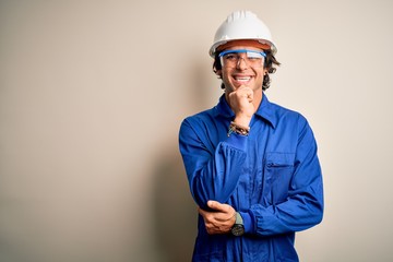 Young constructor man wearing uniform and security helmet over isolated white background looking confident at the camera with smile with crossed arms and hand raised on chin. Thinking positive.