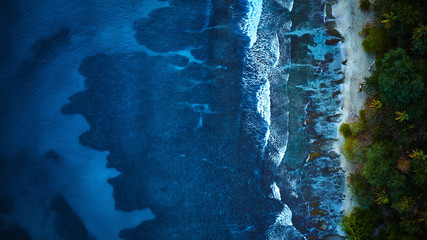 Scenic aerial shot of a sunny beach with white sand surrounded by transparent blue ocean water.