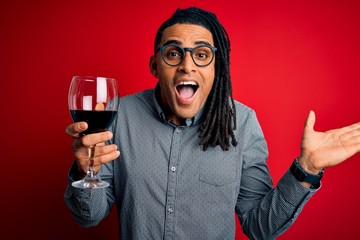 Young african american afro sommelier man with dreadlocks drinking glass of wine very happy and...