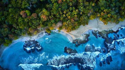 Magnificent aerial shot of a blue tropic lagoon with crystal clear water surrounded by beach and palm trees.