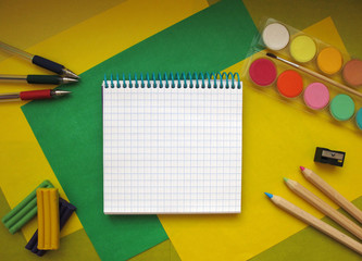 Top view of school stationery: paints, colored pencils, pens, notepad on a background of colored paper. Back to school flat lay with copy space