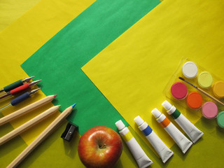 Top view of school stationery: paints, colored pencils, pens and apple on a background of colored paper. Back to school flat lay with copy space