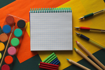 Fototapeta na wymiar Top view of school stationery: paints, colored pencils, pen, plasticine and muffin on a background of colored paper. Back to school flat lay with copy space