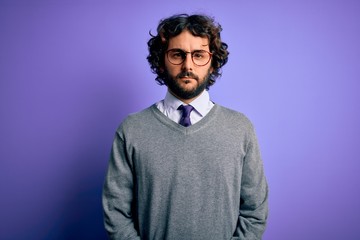 Handsome businessman with beard wearing tie and glasses standing over purple background with serious expression on face. Simple and natural looking at the camera.