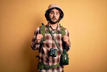 Young hiker man with curly hair and beard hiking wearing backpack and water canteen In shock face,...