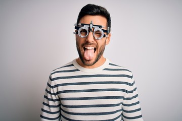 Young handsome man with beard wearing optometry glasses over isolated white background sticking tongue out happy with funny expression. Emotion concept.