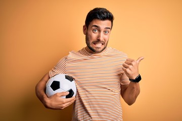 Handsome player man with beard playing soccer holding footballl ball over yellow background...