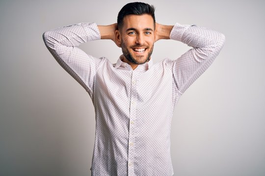 Young handsome man wearing elegant shirt standing over isolated white background relaxing and stretching, arms and hands behind head and neck smiling happy