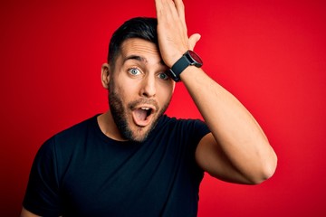 Young handsome man wearing casual black t-shirt standing over isolated red background surprised with hand on head for mistake, remember error. Forgot, bad memory concept.