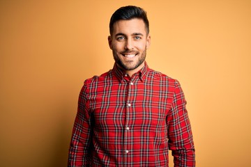 Young handsome man wearing casual shirt standing over isolated yellow background with a happy and cool smile on face. Lucky person.