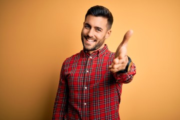 Young handsome man wearing casual shirt standing over isolated yellow background smiling friendly...