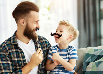 Father and son having fun with mustache at home