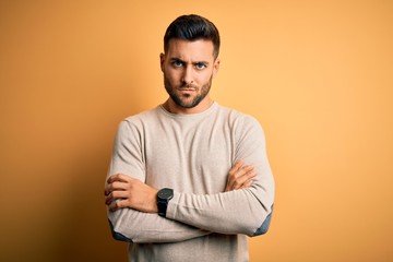 Young handsome man wearing casual sweater standing over isolated yellow background skeptic and nervous, disapproving expression on face with crossed arms. Negative person.