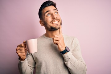 Young handsome man drinking a cup of hot coffee over pink isolated background serious face thinking...