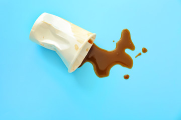 Overturned paper cup and spilled coffee on color background