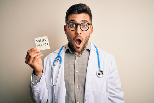Young doctor man wearing stethoscope holding virus alert note over isolated background scared in shock with a surprise face, afraid and excited with fear expression