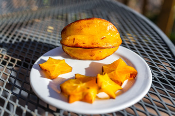 Closeup of sliced orange yellow starfruit on plate on metal table outside with vibrant color