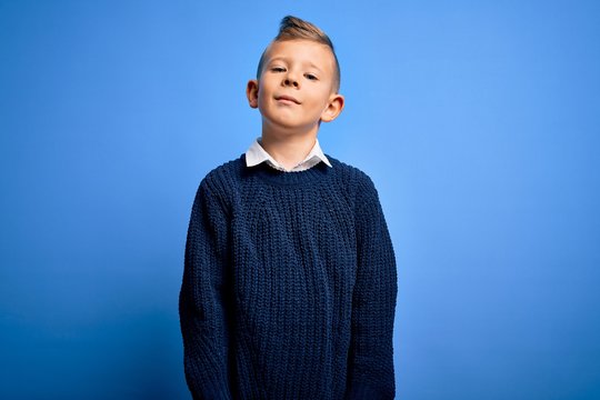 Young little caucasian kid with blue eyes wearing winter sweater over blue background Relaxed with serious expression on face. Simple and natural looking at the camera.