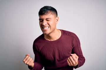 Young handsome hispanic man wearing casual shirt standing over white isolated background very happy and excited doing winner gesture with arms raised, smiling and screaming for success. Celebration