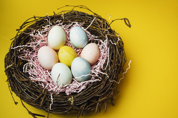 A nest of twigs and hay and a pink paper filler with pastel colored Easter eggs. Colored eggs for the holiday of light Easter. Easter card on a yellow background