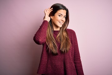 Young beautiful girl wearing casual sweater over isolated pink background smiling with hand over ear listening an hearing to rumor or gossip. Deafness concept.