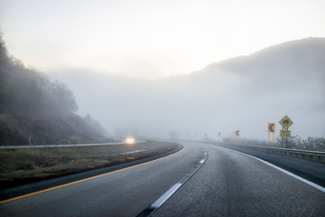 Foggy mist road highway driving with headlights in rural countryside in West Virginia with cars and...