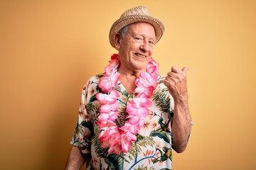 Grey haired senior man wearing summer hat and hawaiian lei over yellow background smiling with...