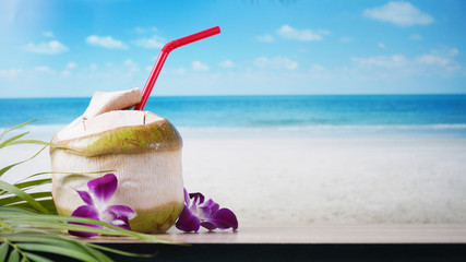 Fresh coconut water on table and blurred beach summer background.