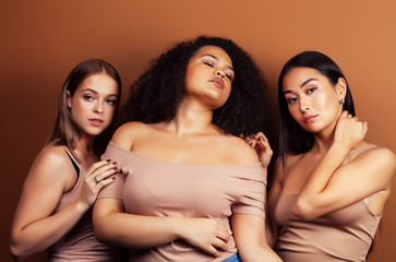 Obraz premium young pretty asian, caucasian, afro woman posing cheerful together on brown background, lifestyle diverse nationality people concept