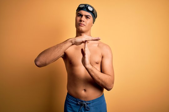 Young handsome man shirtless wearing swimsuit and swim cap over isolated yellow background Doing time out gesture with hands, frustrated and serious face