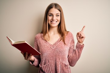 Young beautiful redhead student woman reading book over isolatated white background surprised with an idea or question pointing finger with happy face, number one