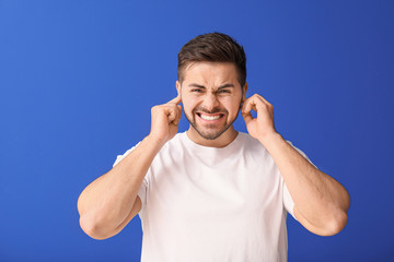 Young man suffering from loud noise on color background