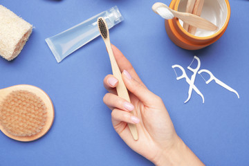 Female hand with wooden tooth brush and bath supplies on color background
