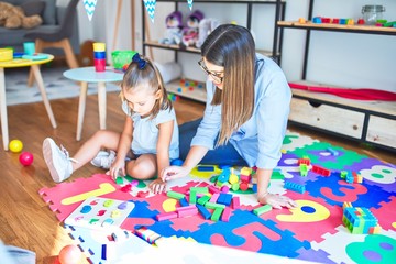 Caucasian girl kid playing and learning at playschool with female teacher. Mother and daughter at playroom around toys playing with bulding blocks